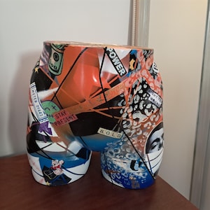 May include: A decorative torso sculpture with a vibrant, abstract design. The sculpture features a mix of colors including orange, blue, and white, with text elements like "POWER", "BOLD", and "STAY PRESENT".
