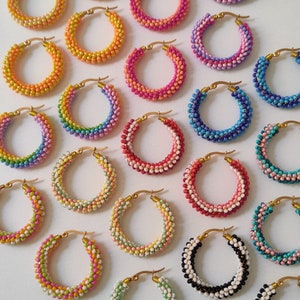 Op de afbeelding: Een verzameling kleurrijke kralen oorringen. De oorringen zijn gemaakt met kleine kralen in verschillende kleuren, waaronder roze, blauw, groen, geel en zwart. De hoepels zijn allemaal even groot en zijn gemaakt van goudkleurig metaal.