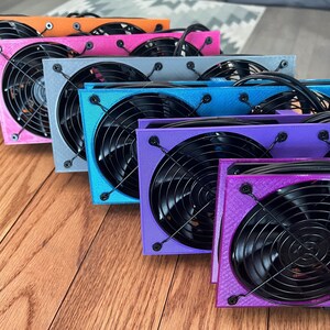 May include: Six 3D printed fan housings in different colors, including orange, pink, gray, blue, purple, and a darker purple. Each housing has two fans with black blades and a black mesh grill.