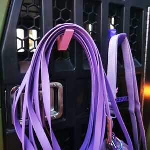 Puede incluir: Correas moradas colgando de un gancho rosa sujeto a una jaula de perro de metal negro. La jaula tiene una placa plateada con el texto "Ducks Unlimited" en ella.