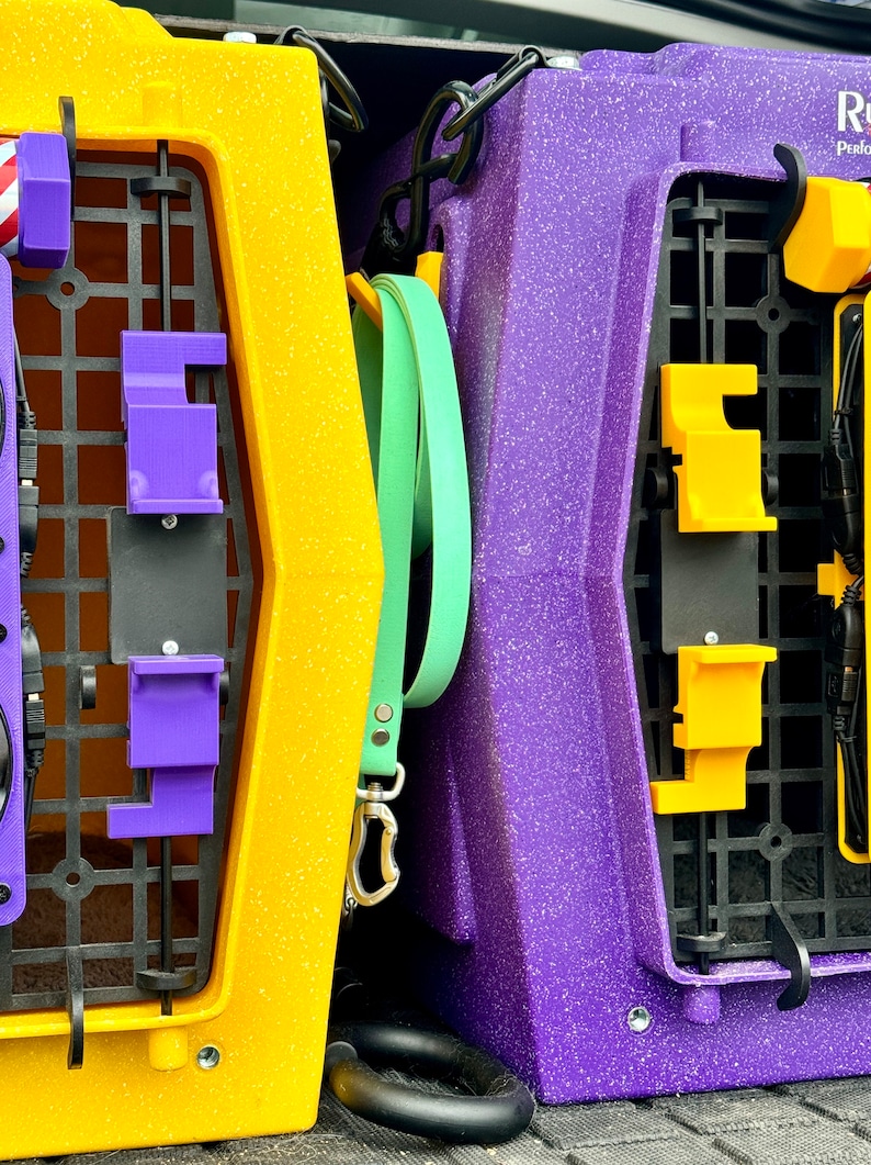 May include: Two pet carriers, one yellow and one purple, are stacked on top of each other in the back of a vehicle. The yellow carrier has a purple latch and a green leash attached to it. The purple carrier has a yellow latch.