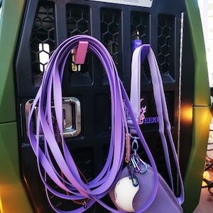 Puede incluir: Una jaula de perro de metal verde con una puerta de metal negro y una correa morada colgando de un gancho. La jaula tiene una placa de nombre plateada que dice "Ducks Unlimited". Hay una bolsa morada con una pelota blanca dentro colgando de otro gancho. La jaula tambi&eacute;n tiene una placa de nombre plateada que dice "Gunner".