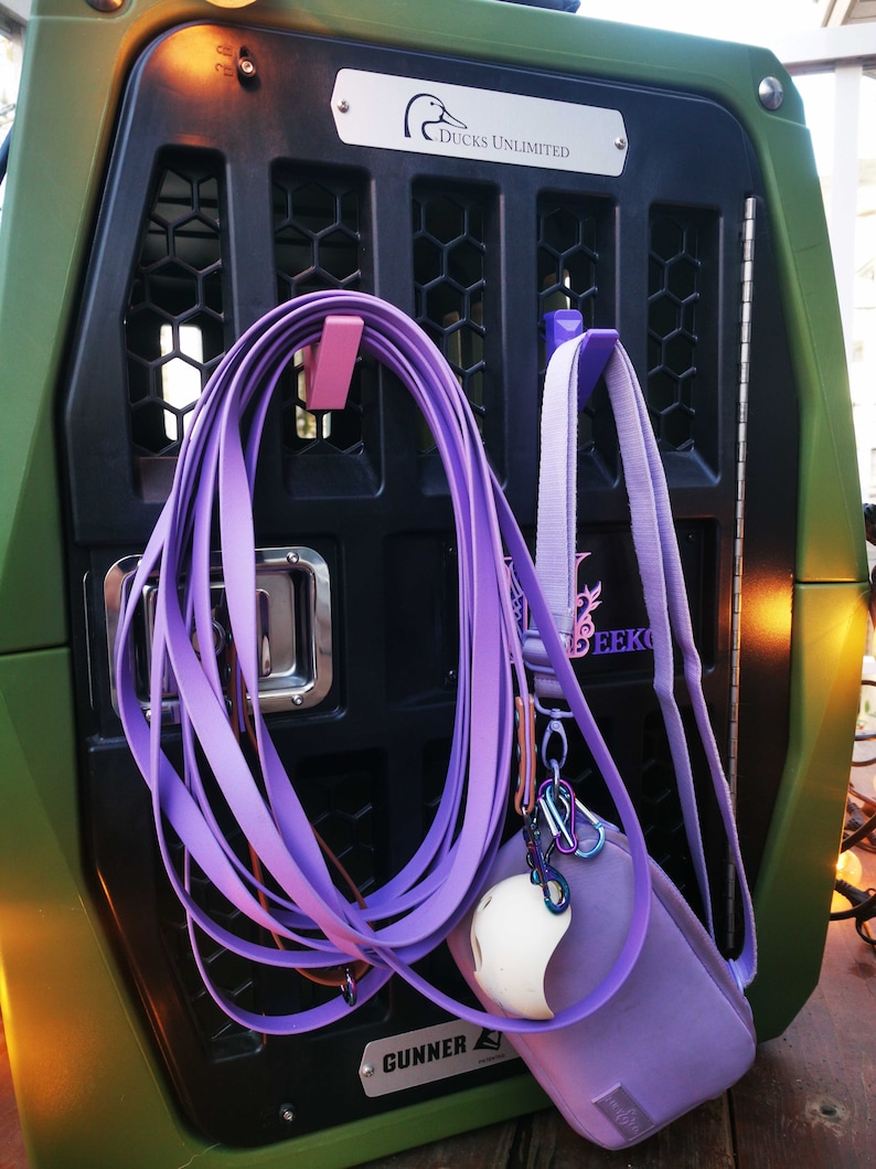 Puede incluir: Una jaula de perro de metal verde con una puerta de metal negro y una correa morada colgando de un gancho. La jaula tiene una placa de nombre plateada que dice "Ducks Unlimited". Hay una bolsa morada con una pelota blanca dentro colgando de otro gancho. La jaula tambi&eacute;n tiene una placa de nombre plateada que dice "Gunner".