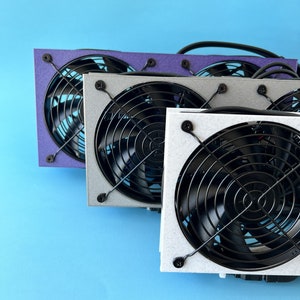 May include: Three computer cooling fans with black grills and different colored frames. The fans are stacked on top of each other, with the purple frame on top, the gray frame in the middle, and the white frame on the bottom.