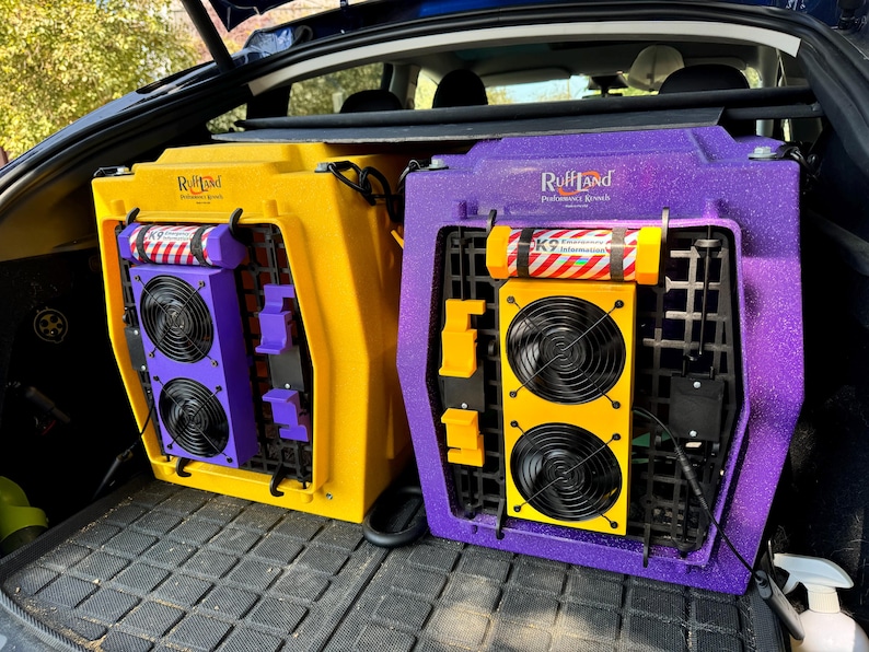 Pu&ograve; includere: Due trasportini per animali domestici con ventilatori incorporati. Il trasportino a sinistra &egrave; giallo con dettagli viola e il trasportino a destra &egrave; viola con dettagli gialli. Entrambi i trasportini hanno la scritta "RuffLand Performance Kennels" stampata su di essi.