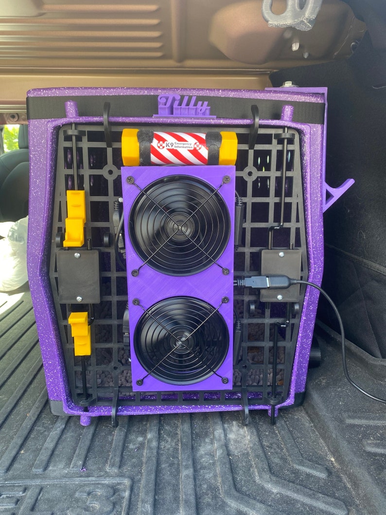 May include: Purple pet carrier with a black strap and a black and yellow handle. The carrier has two black fans attached to the front with a black cord plugged into the side. The text "Tilly" is printed on the top of the carrier.