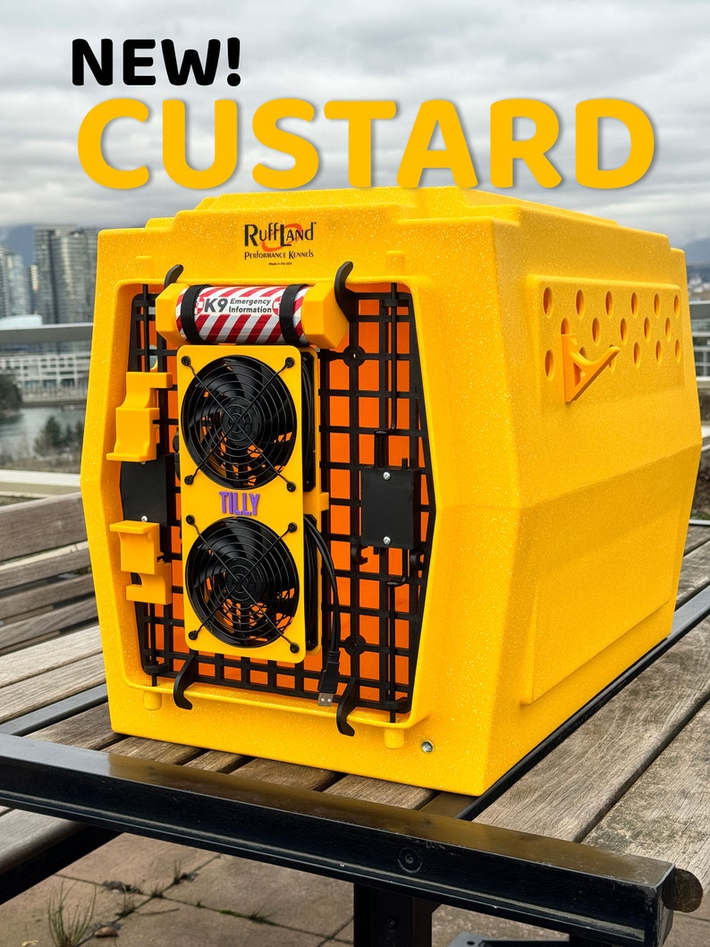May include: A yellow Ruffland Performance Kennels dog crate with a black metal door and two black fans. The crate has a white sticker with the text "K9 Emergency Information" and a purple sticker with the text "Tilly". The crate is sitting on a wooden table.