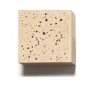 Puede incluir: Un sello de madera con un diseño moteado en blanco y negro. El sello es cuadrado y tiene un color marrón claro.