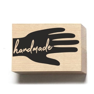May include: A wooden stamp featuring a black silhouette of a hand with the word "handmade" written in cursive.