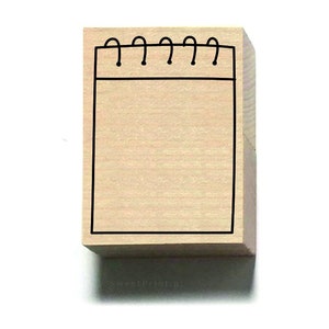 Könnte beinhalten: Ein Holz-Stempel mit einer schwarzen Umrandung eines Notizbuchs mit einer Spiralbindung.