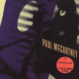 May include: A purple and yellow album cover with a black and white photo of Paul McCartney. The album title is "Unplugged Deluxe" and the text "the complete performances and more" is below the title. The album cover also includes the text "Limited Edition" and "2 CD's and 2 DVD".