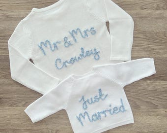 May include: Two white knit sweaters. One sweater has the text "Mr & Mrs Crowley" embroidered in light blue. The other sweater has the text "Just Married" embroidered in light blue. Both sweaters have long sleeves.