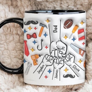 May include: White ceramic mug with a black rim and handle. The mug features a design of a father and three children's hands in a fist bump, surrounded by various icons including a tie, bowtie, hammer, wrench, fishing hook, and a football. The text "Dad" is written on the mug, along with the names "Jayden", "James", and "Olivia".