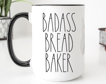 May include: White ceramic mug with a black rim and handle. The mug has the text "Badass Bread Baker" printed in black.
