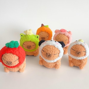 May include: Six plush toys wearing different animal-themed hats. The hats are a green frog, a red apple, a white panda, an orange pumpkin, a pink pig, and a yellow banana. The toys are all brown and have a soft, fuzzy texture.