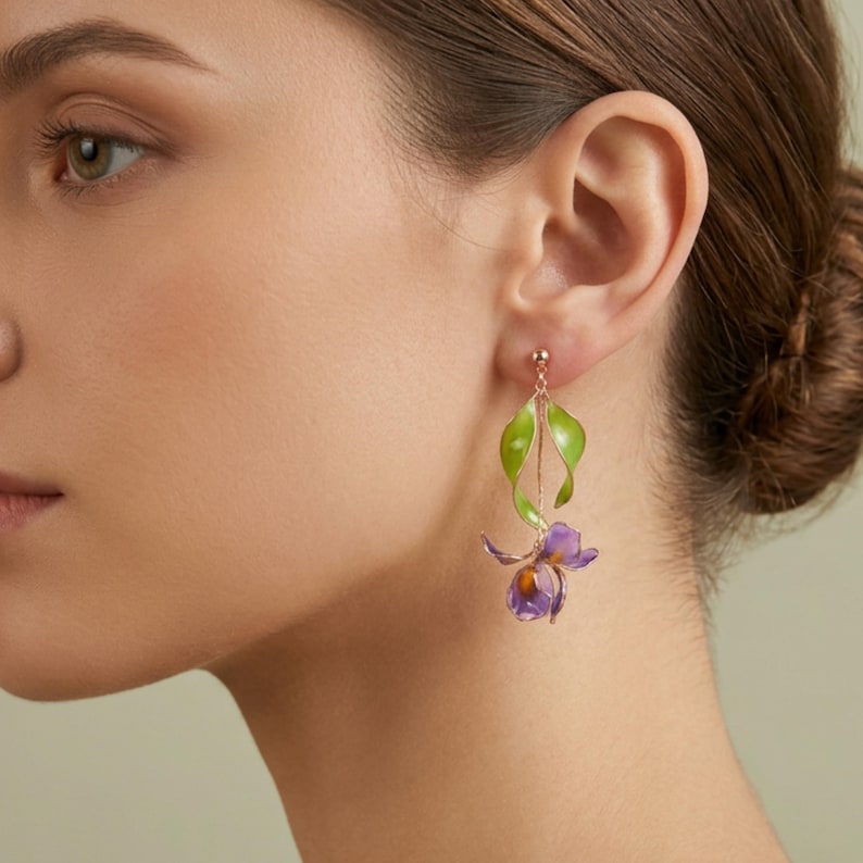 May include: A drop earring featuring a gold-toned post and a delicate chain connecting a bright green leaf element to a purple and orange iris flower pendant. The design hangs vertically from the earlobe with a slender, elegant profile.