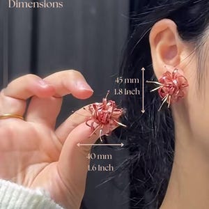 May include: A pair of pink flower-shaped earrings. The earrings are 1.8 inches (45 mm) and 1.6 inches (40 mm) in diameter.