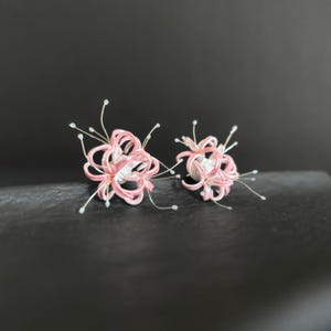 May include: A pair of pink and white flower earrings with delicate silver wire details. The flowers are made of fabric and have a delicate, feminine look.