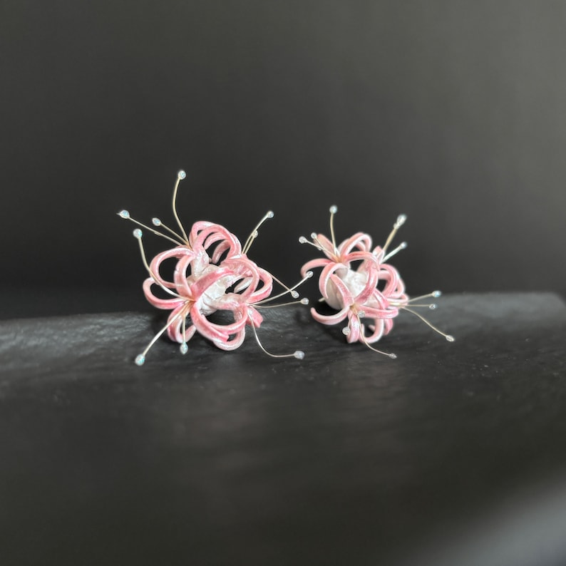 May include: A pair of pink and white flower earrings with delicate silver wire details. The flowers are made of fabric and have a delicate, feminine look.