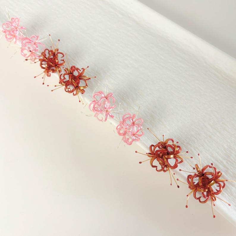 May include: A set of six delicate wire flower hair clips in shades of pink and copper. The flowers are arranged in a cluster and have a delicate, airy appearance.