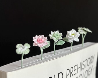 Puede incluir: Cinco marcapáginas de ganchillo en forma de flores en tonos de rosa, blanco y verde se colocan en un libro. El libro se titula "World Prehistory Archaeology".