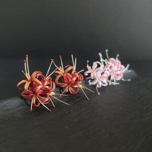May include: Two pairs of red and gold flower earrings and one pair of pink and white flower earrings. The earrings are made of silk and are shaped like a cluster of flowers.