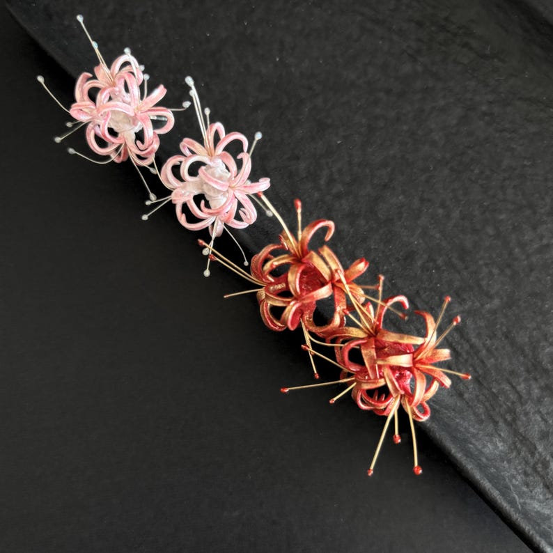 May include: Three delicate flower hair clips in pink and red with gold accents. The flowers are made of paper and have a delicate, intricate design.