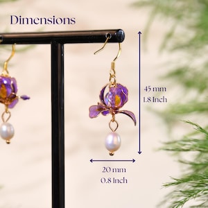 May include: A pair of gold-toned hook earrings featuring purple translucent flower petals and a dangling white pearl. The text Dimensions is visible, with measurements of 1.8 inches in height and 0.8 inches in width indicated by arrows.