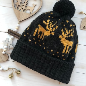 May include: Black knit beanie with a yellow reindeer pattern and a black pom pom on top.