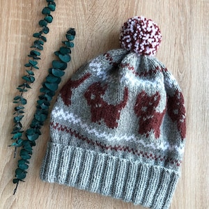 May include: A grey knitted hat with a brown and white pattern and a pink and white pom pom on top.
