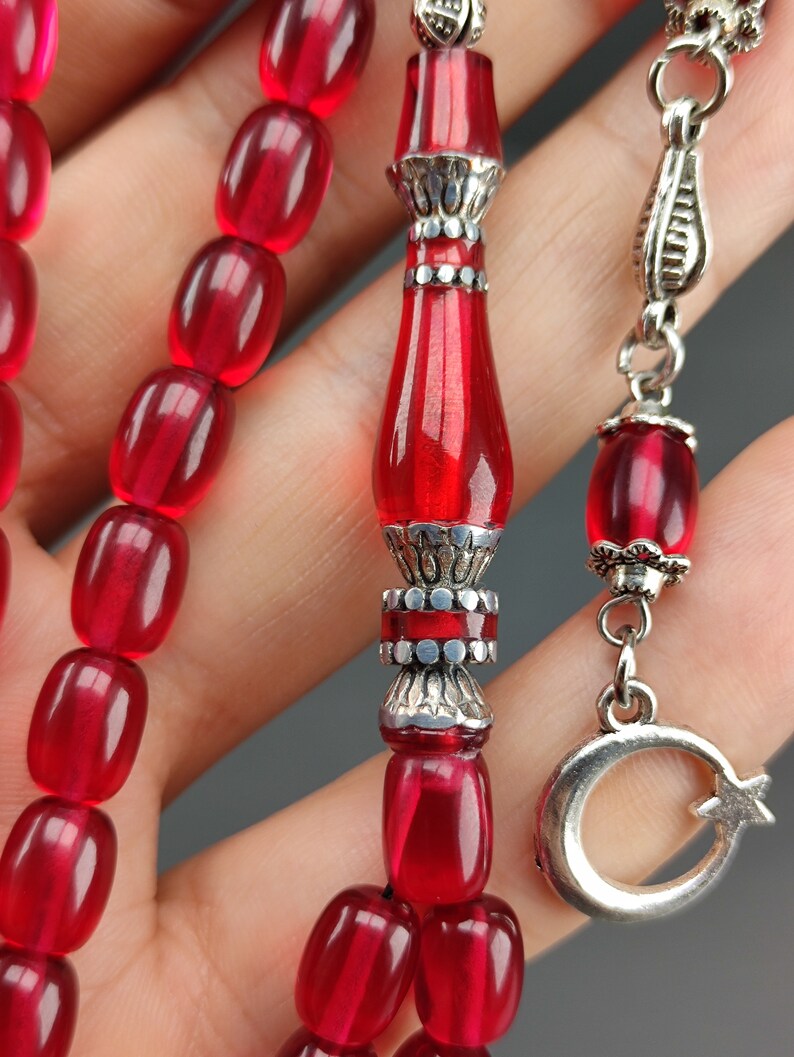 May include: A red prayer beads necklace with silver accents. The beads are oval shaped and the pendant is a crescent moon with a star.