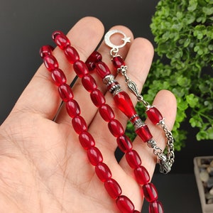 May include: A red prayer beads necklace with silver accents. The beads are oval shaped and the necklace has a silver tassel and a crescent moon charm.