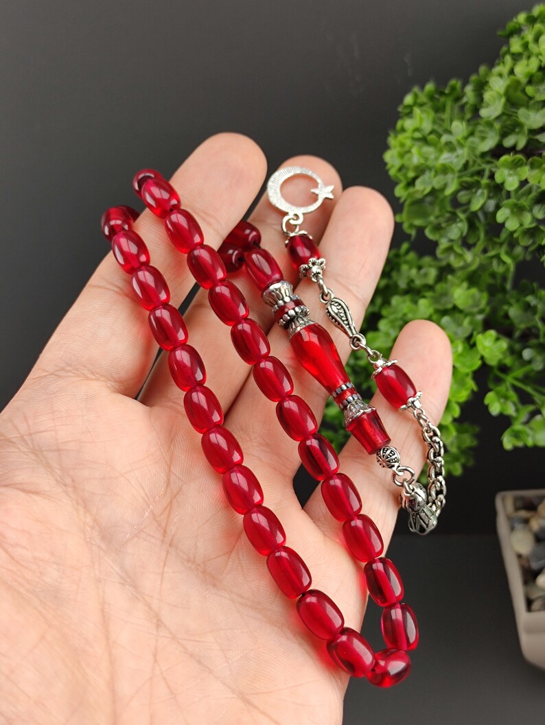May include: A red prayer beads necklace with silver accents. The beads are oval shaped and the necklace has a silver tassel and a crescent moon charm.