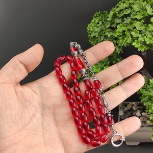May include: A red glass prayer bead mala with silver accents. The mala has a tassel with a crescent moon and star charm.