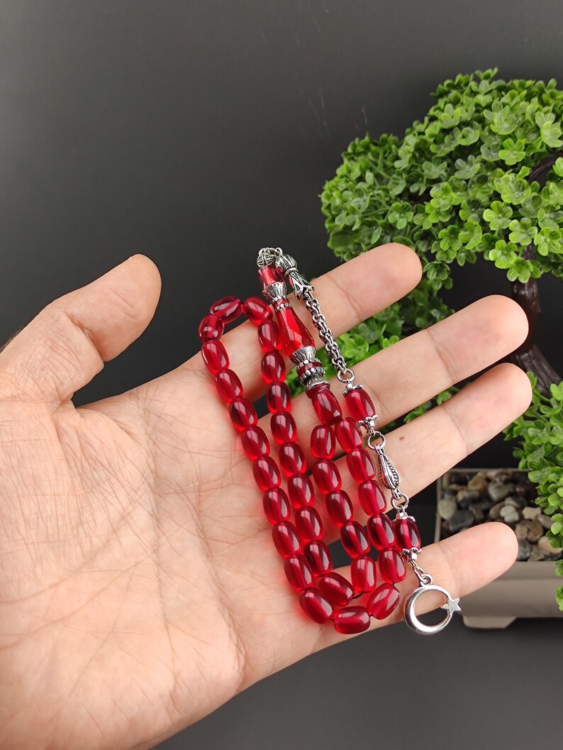 May include: A red glass prayer bead mala with silver accents. The mala has a tassel with a crescent moon and star charm.