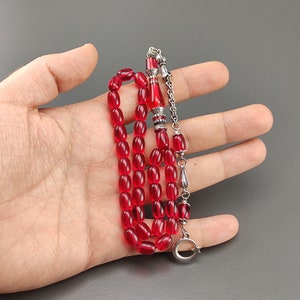 May include: A red prayer beads necklace with silver accents. The beads are oval shaped and the necklace has a silver tassel.