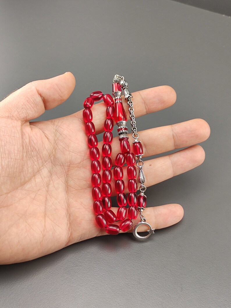 May include: A red prayer beads necklace with silver accents. The beads are oval shaped and the necklace has a silver tassel.