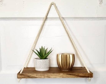 May include: A wooden shelf with rope hangers, a small potted succulent plant, and a gold striped candle holder.