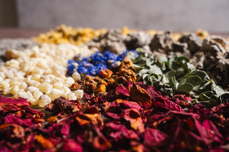 Op de afbeelding: Een close-up van diverse gedroogde kruiden en botanische producten. De afbeelding toont een verscheidenheid aan kleuren, waaronder rood, wit, blauw, geel en groen. De opstelling suggereert een verzameling ingredi&euml;nten voor aromatherapie of kruidenremedies.