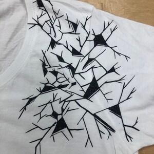 May include: White t-shirt with a black graphic design of a geometric pattern resembling a cracked or broken surface.