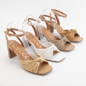 May include: Three pairs of women's heeled sandals with knotted straps. The sandals are in beige, white, and brown.