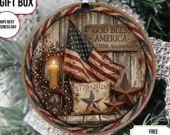 Op de afbeelding: Een ronde hangende decoratie met een rustieke houten achtergrond, een bedrukte Amerikaanse vlag, een brandende gele kaars, een bessenkrans en een kussen met de tekst 1776-2026. Een houten bordje toont de tekst GOD BLESS AMERICA- 250th Anniversary.