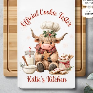 May include: White kitchen towel with a cartoon Highland cow wearing a chef's hat and scarf, holding a star-shaped cookie. Text reads "Official Cookie Tester" and "Katie's Kitchen" in red. Includes options for font, microfiber waffle, or flat cotton.