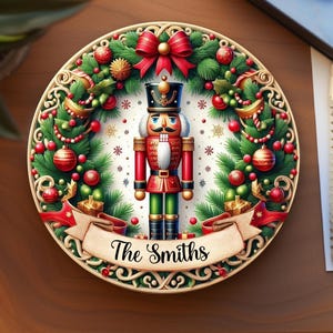 May include: A decorative round plate featuring a Christmas nutcracker soldier in a red, green, and black uniform. The plate is surrounded by a festive wreath with red ornaments, a red bow, and the text "The Smiths" on a banner.