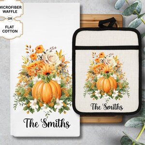 May include: A white kitchen towel and oven mitt set featuring a watercolor design of a pumpkin and floral arrangement in orange, yellow, and white. The text "The Smiths" is printed on both items. The towel offers a choice of microfiber waffle or flat cotton.