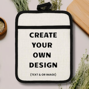 May include: A white pot holder with a black border and handle. The text "CREATE YOUR OWN DESIGN (TEXT & OR IMAGE)" is printed in black. The pot holder is surrounded by herbs and a wooden chopping board.