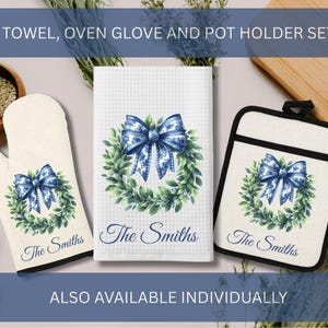 以下が含まれることがあります： 白いワッフル織りのタオル、オーブンミトン、鍋つかみがセットになったキッチンセット。各アイテムには、青いリボンとリース模様に「The Smiths」の文字がデザインされています。このセットはキッチンでの使用を目的としています。