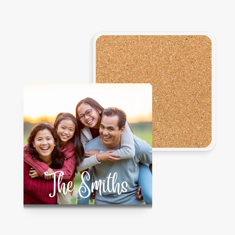 A square photo coaster with a white border. The coaster features a family of four smiling and looking at the camera. The family is standing in a field with a sunset in the background. The text 'The Smiths' is written in white cursive font below the family.