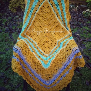 May include: A crocheted throw blanket in a mustard yellow color with a diamond pattern in the center. The blanket has a blue and peach border with a scalloped edge.