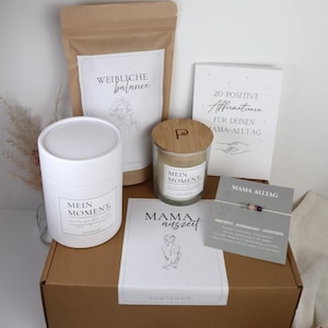 Könnte beinhalten: Eine Geschenkbox mit einer weißen Kerze, einer Kerze im Glas mit Holzdeckel, einem Teebeutel, einer Karte mit Affirmationen, einer Karte mit einem Armband und einer Karte mit der Aufschrift "Mama Auszeit". Auf der Box steht das Wort "PANTERSIE".